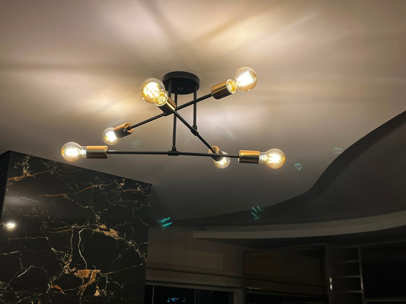 Lustre decorativo de seis lâmpadas instalado sobre parede de mármore
